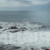 Slow Motion Pan Right of Waves Crashing Over Rocks in Stone Shoreline Landscape, Evoking a Sense of Freedom. Cloudy Skies in Distant Background.